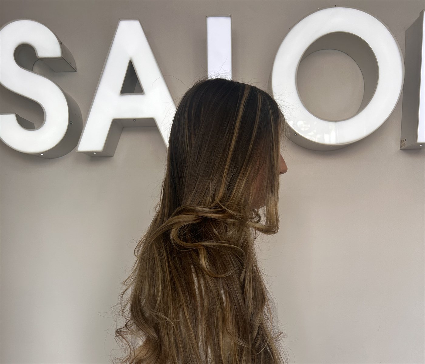 Honey-blonde layered waves in front of the Frenzy Salon sign